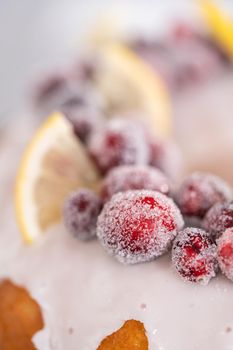 Lemon cranberry bundt cake decorated with sugar cranberries and lemon wedges on a cake stand.