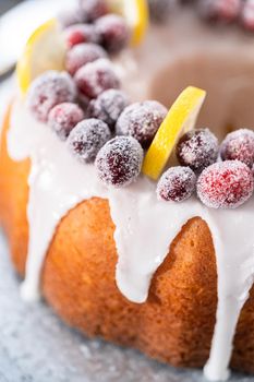 Lemon cranberry bundt cake decorated with sugar cranberries and lemon wedges on a cake stand.