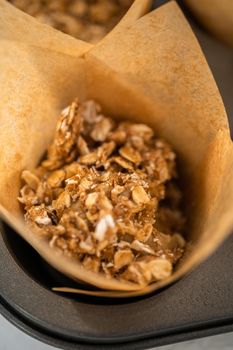 Scooping dough with dough scoop into cupcake pan lined with tulip paper muffin liners to bake banana oatmeal muffins.