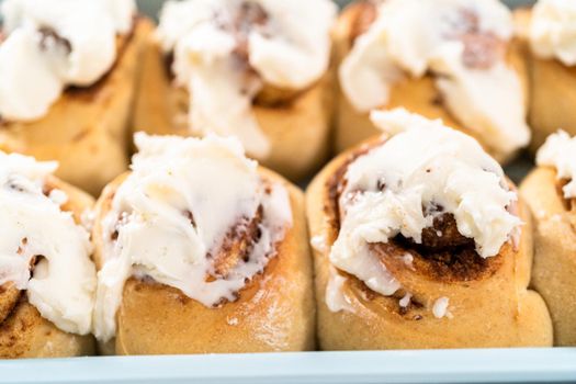 Freshly baked cinnamon rolls with white icing in a blue baking pan.