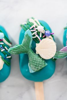 Mermaid cakesicles with drizzled chocolate, chocolate mermaid tails, seashells, and sprinkles.