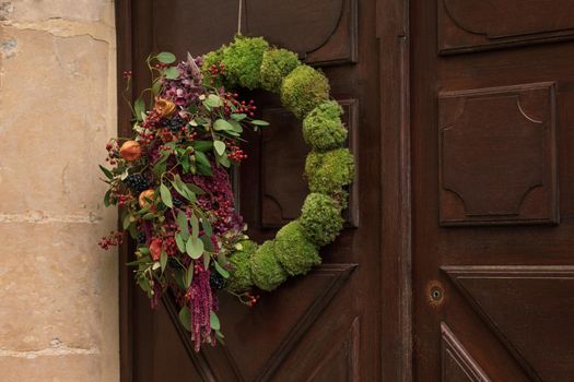 Wreath with the red berries and the dry leaves and fruits hanging on a door.