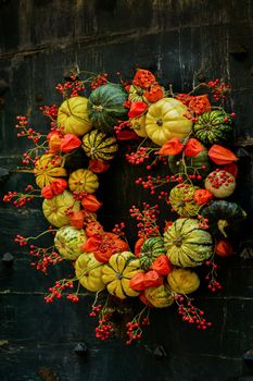 Handmade wreath of small pumpkins and zucchini on a black vintage door