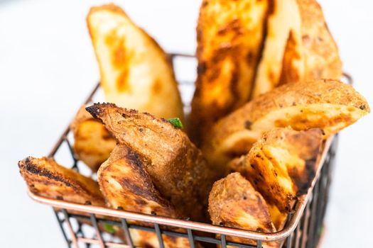 Freshly baked potato wedges with spices in a wire basket.