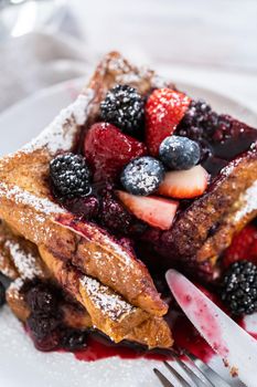 Stack of freshly made french toast garnished with mix berry compote and powder sugar.