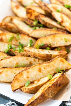 Freshly baked potato wedges with spices on a white serving tray.