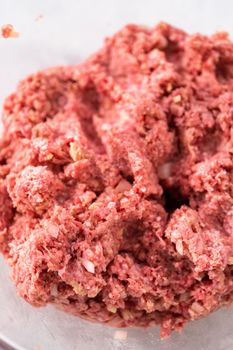 Mixing ingredients with hands in a glass mixing bowl to make meatloaf.