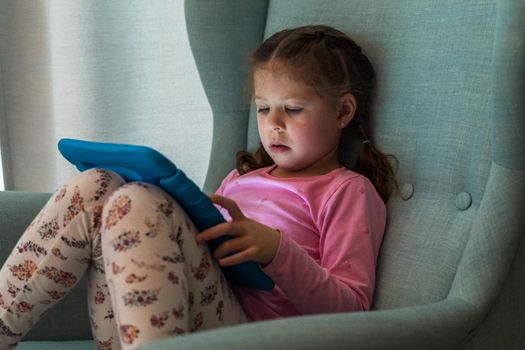 Little girl reading books on her tablet at homeschool.