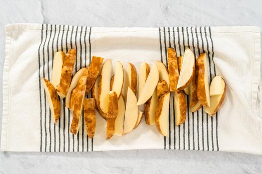 Flat lay. Preparing russet potatoes in wedges with olive oil and spices to bake in the oven.