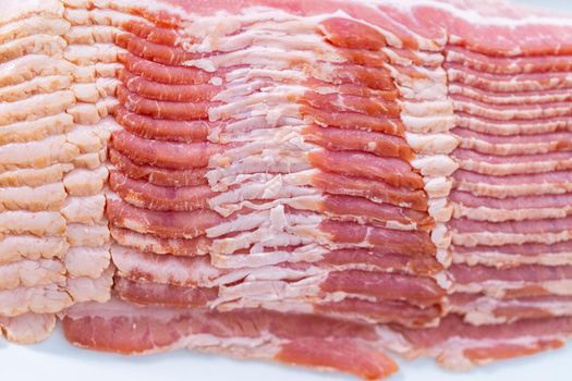 Uncooked bacon strips on a large white plate.