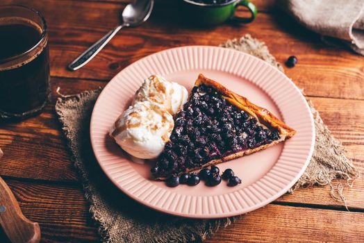 Slice of Homemade Serviceberry Pie and Two Scoops Of Vanilla Ice Cream on Plate over Wooden Table