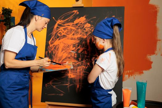 Adult and kid using orange paint on canvas, painting artistic masterpiece with watercolor aquarelle, wet paint from palette and paintbrush. Creating colorful artwork with skills and creative vision.