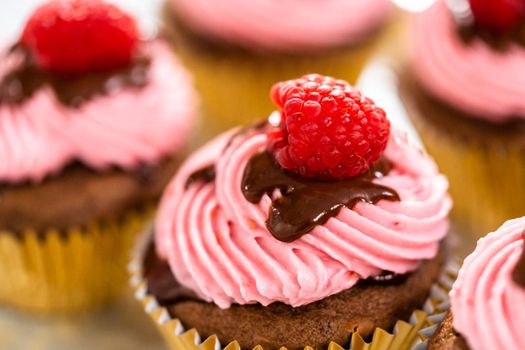 Gourmet chocolate raspberry cupcakes drizzled with chocolate ganache and topped with a fresh raspberry.