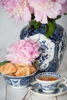 spring still life with croissants and a bouquet of pink luxurious peonies in an ancient Chinese vase with blue ornament, an antique tea cup, early breakfast or brunch, High quality photo