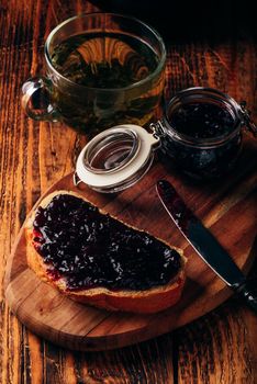 Toast with berry jam on cutting board and cup of green tea