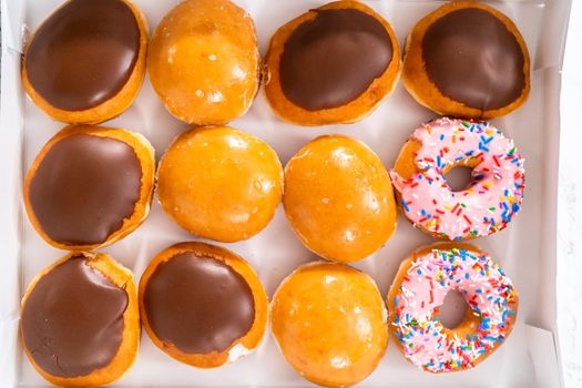 Variety of store-bought doughnuts in a white paper box.