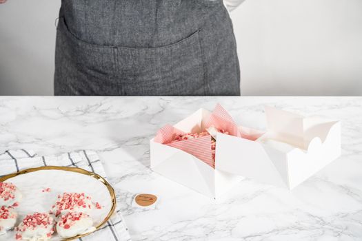 Packing freshly baked peppermint white chocolate cookies into a white paper box.