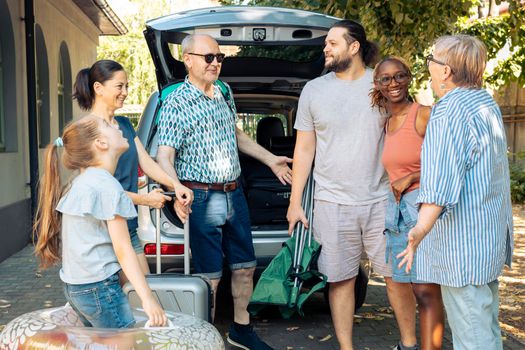 Multiethnic people loading bags in vehicle trunk, travelling on holiday vacation at seaside with multiethnic family and friends. Leaving on adventure journey with luggage, suitcase and inflatable.