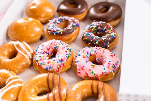 Variety of store-bought doughnuts in a white paper box.