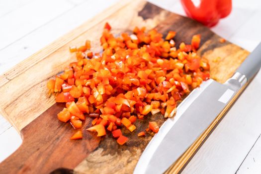 Mincing organic red bell peppers on a wood cutting board.