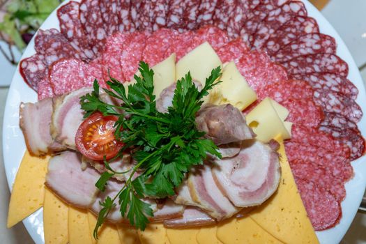 A plate of cold appetizers with various sausages, meat, and cheese. Greens and tomatoes