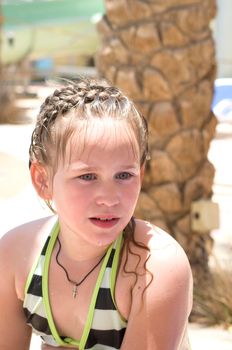 portrait of a little girl in a striped swimsuit with wet hair who swam in the pool in summer. High quality photo