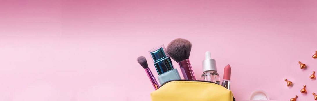 Top view of set of make up and skin care products spilling out of cosmetics bag on blue background. Beauty concept.