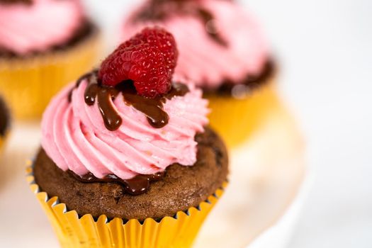 Gourmet chocolate raspberry cupcakes drizzled with chocolate ganache and topped with a fresh raspberry.