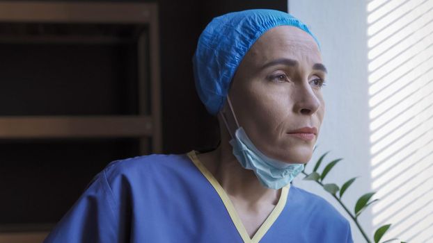 Tired Medic Looks At Window Took Off Her Mask, Female Doctor In Protective Uniform Exhausted By Work During An Outbreak Of Corona Virus, Woman Hope For A Better Future, Pandemic Concept