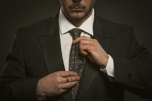 Man in black suit hols necktie. Beautiful portrait for clothing design. Business concept. Black background.