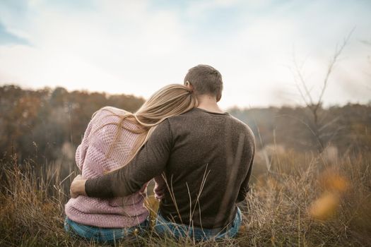 Rear View of hugging tourists sitting on the edge of a cliff inhaling the aromas of autumn nature outdoors, Healthy Lifestyle concept.