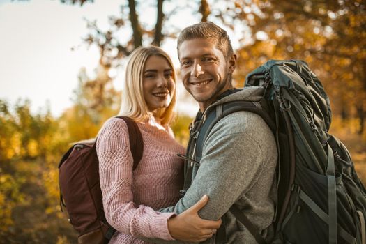 Happy couple of backpackers hugging while looking at the camera, a Caucasian couple in love toothy laughs while standing against the backdrop of colorful autumn nature.