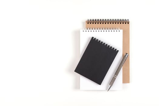 Three blank notepads on a spiral stacked in a stack on a white background. Notebooks with white, black and recycled sheets and pen. Education, office.