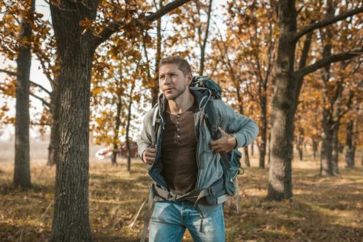 Tourist at the beginning of the journey. An inspired guy with a big backpack got out of a red car and begins his journey through the autumn forest. Hiking concept.