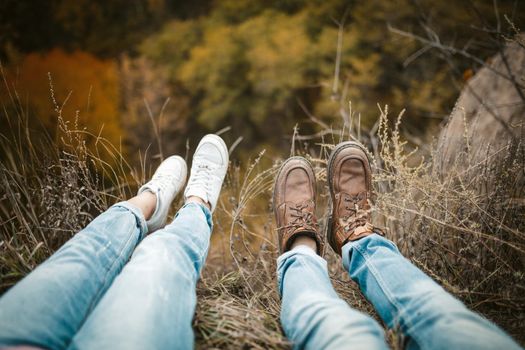 Male and female legs in tourist shoes sitting on a cliff, Young man and a woman are sitting on the edge hanging legs down, high angle view