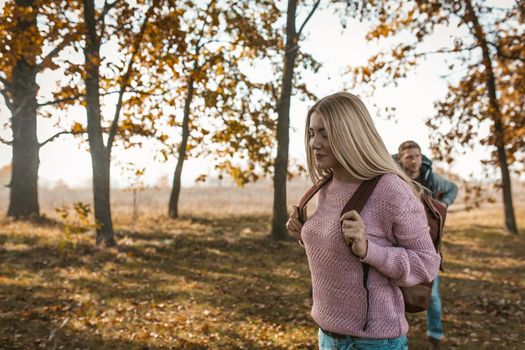 Happy Travelers with backpacks begins their journey in the autumn Sunny forest, Focus on smiling beautiful blonde with long hair in the foreground.