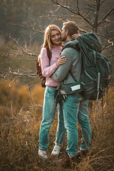 Couple In Love Rest Stopping On The Edge Of Cliff, Young Backpackers Hug And Kiss On Background Of Beautiful Autumn Nature, Caucasian Man And Beautiful Blonde Are Hiking Together