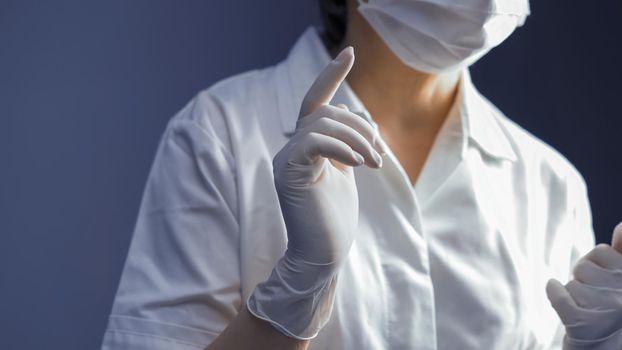 Woman wearing white latex gloves and medical uniform. Focus on female hand in foreground. Close up shot. Hygiene concept. Tinted image.