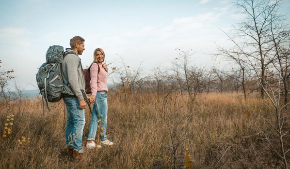 Hiking Of Loving Travelers Holding Hands, Young Caucasian Man And Woman In Casual Clothes Walking In Autumn Meadow Outdoors, Hiking Concept