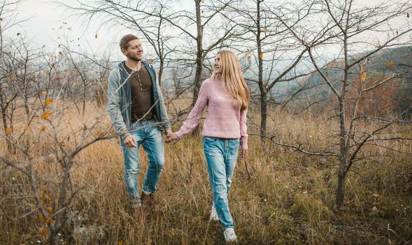 Man and woman walking together in nature outdoors. Two people in love are walking along the hillside holding hands.