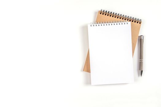 Two blank spiral notepads stacked on a white background next to an automatic pen. Notebooks with white and recycled sheets. Education, office.