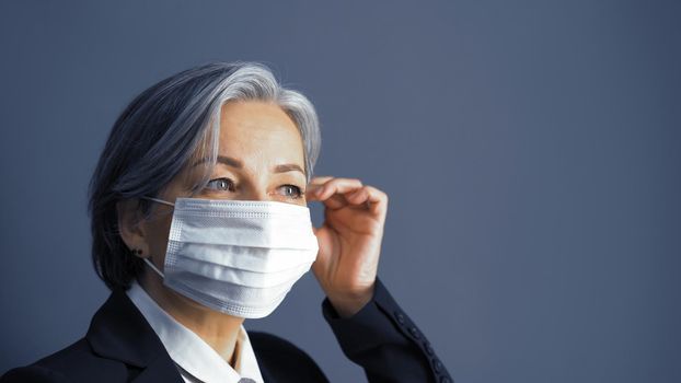 Pretty gray-haired business woman correct mask on her face. Focus on female eyes. Middle-aged Caucasian woman on blue gray background. Copy space at right. Close up portrait. Toned image.