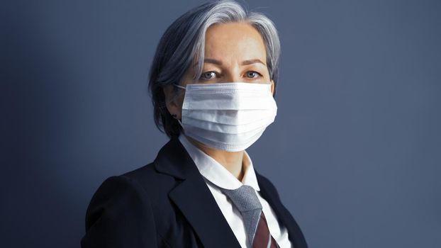 Serious graying businesswoman in mask. Close up portrait of caucasian middle-aged looking at camera. Text space on both sides. Toned image. Business concept. Quarantine concept.