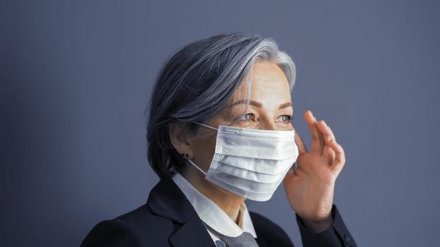 Mature business woman correct mask on her face. Focus on female eyes. Portrait of gray-haired woman on blue gray background. Close up shot. Toned image.