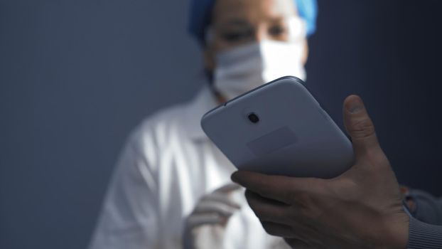 Female doctor or nurse learning to use an electronic notepad gadget. Focus on electronic device in male hands in the foreground. Education concept. Close up shot. Toned image.