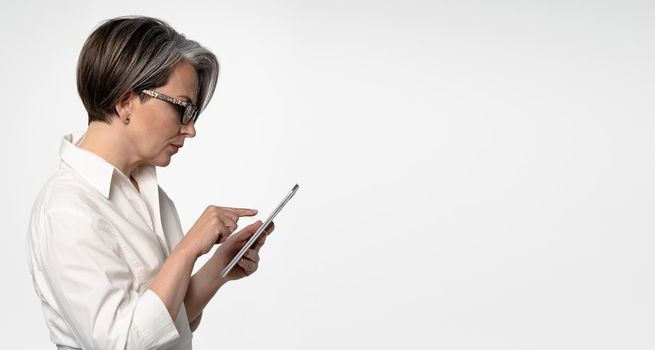 Gray-haired Caucasian businesswoman typing on tablet computer on white background. Horizontal template for ad banner with textspase at right.