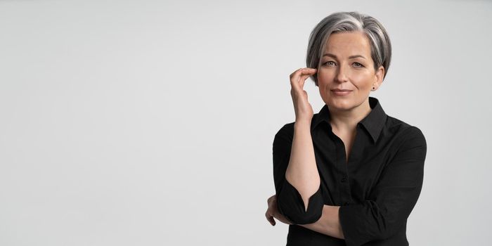 Beautiful gray-haired Caucasian woman smiles touching her face with hand. Anti aging skin care concept. Cut out on white background. Horizontal template for ad banner. Textspase at left side.