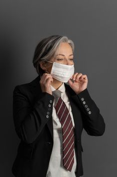 Sad mature woman wearing business suit corrects protective mask on her face. Business during quarantine period.