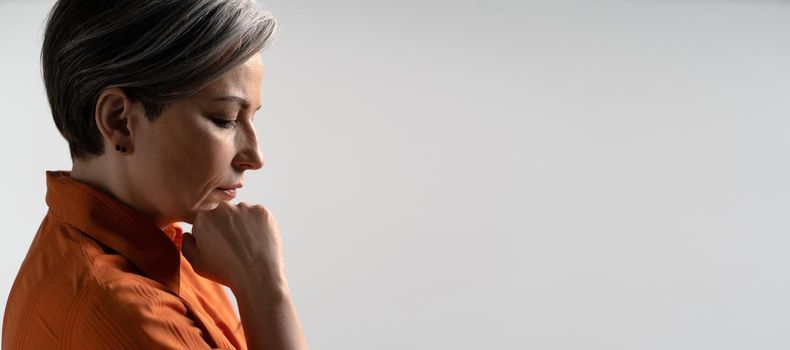 Sad or depressed mature woman thoughtfully touches her chin with hand. Profile view. Copy spase for text. Horizontal template for ad banner.