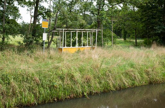 old abandoned bus stop in holland with a small river in front and a lot of high grass instead of the road